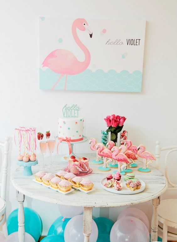 a colorful aqua and pink dessert table with flamingos, pink roses, a polka dot cake and a flamingo art piece