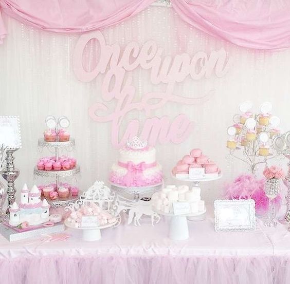 a bright pink dessert table with calligraphy over it, elegant stands with sweets, a castle for decor and horses with a carriage