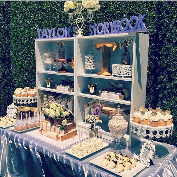 an off-white and grey dessert table with a box-shaped shelf and lots of sweets on stands and even on books