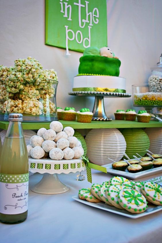 a green and white dessert table with various stands, trays and a sign over it