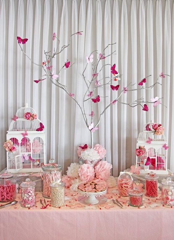 a pink and white baby shower table with vintage cages, a whitewashed tree with pink butterflies, vintage stands with various sweets