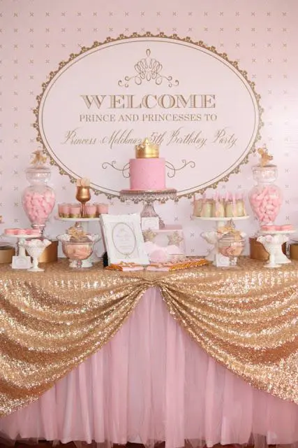 a bright pink and gold dessert table with a letter backdrop, a gold sequin tablecloth, refined stands and bowls
