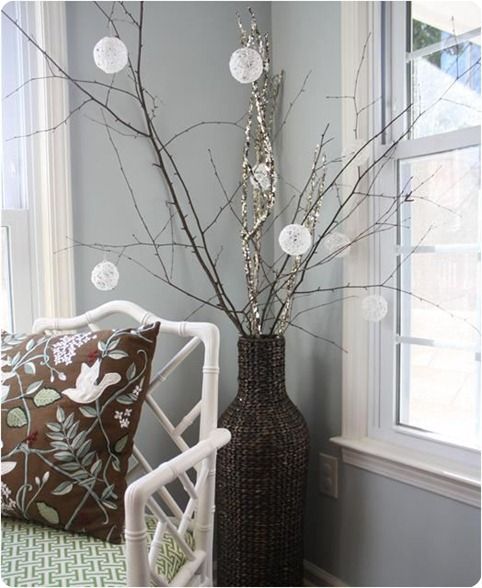 a woven vase with large branches, with lights and snowball ornaments is a pretty and chic decoration for indoors and outdoors