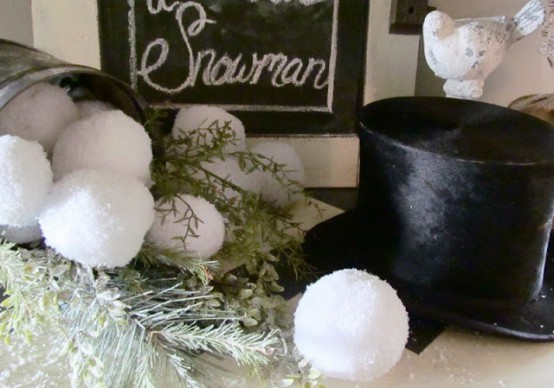 a vintage rustic mantel decorated with a top hat, snowballs, greenery and pale foliage plus a sign is very cozy