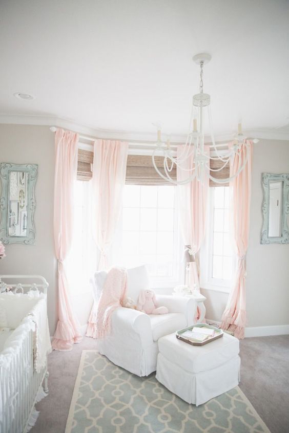 a grey nursery with pink curtains on the bay window, vintage white furniture and touches of mint blue