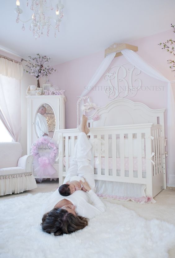 a vintage glam nursery with pink walls, vintage white furniture, a crystal chandelier and touches of pink