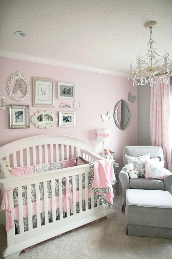 a vintage girl's nursery with pink and grey walls, furniture and bedding, a gallery wall with vintage frames and a crystal chandelier