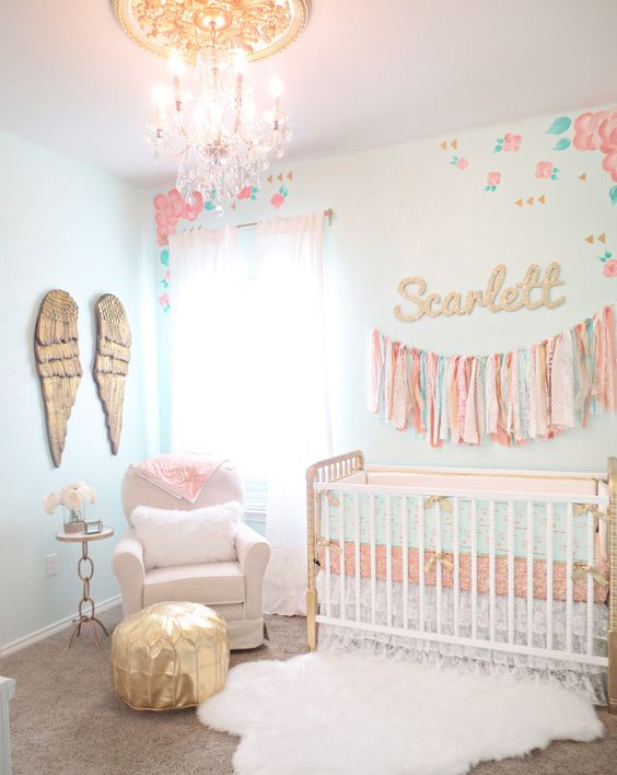 a pastel nurseru with mint walls, a vintage crib, a white chair and a gold ottoman, wings art on the wall and a tassel garland