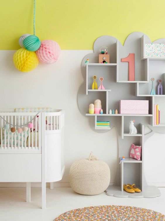 a modern colorful nursery with a color block wall, a grey shelving unit, a white crib and colorful accessories and toys