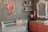 a glam eclectic nurseru with grey and gold polka dot walls, a vintage crib and a dresser, a mirror in a chic frame, open shelves and a floral lamp
