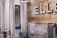 an eclectic nursery with a wood accent wall with marquee letters, shutter windows, pink curtains and a creative chandelier