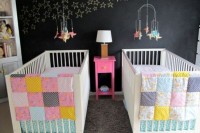 a stylish shared nursery with a chalkboard wall, stars chalked on it, white furniture and colorful patchwork bedding plus colorful mobiles