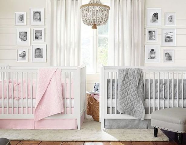 a neutral shared nursery with white walls and furniture, a beaded chandelier, photos and grey and pink bedding