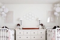 a gender neutral shared nursery with white furniture, white paper lamps, a mother of pearl chandelier and striped bedding