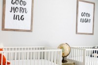 a gender neutral shared nursery with a printed rug, neutral beds, graphic artworks and a gold chest with a globe on it