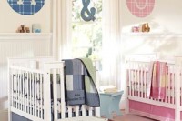 a neutral shared nursery with white paneling and furniture, with blue and pink linens and monograms to highlight each place