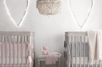 a peaceful neutral shared nursery with grey furniture, light hearts, a crochet chandelier and pink and blue bedding