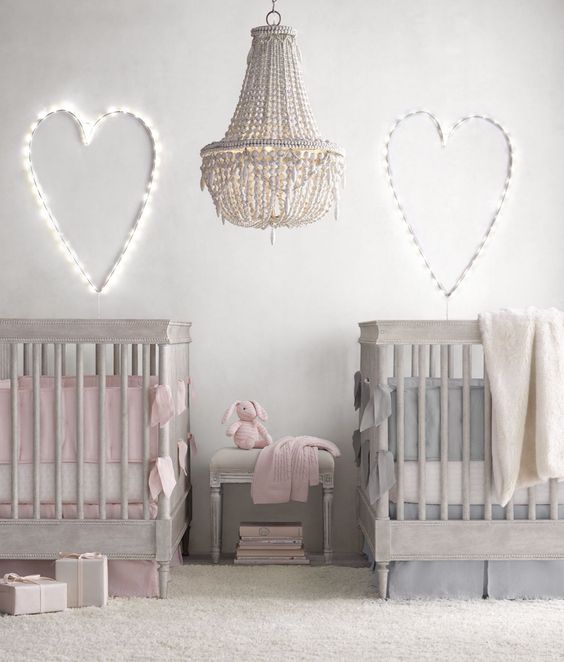 a peaceful neutral shared nursery with grey furniture, light hearts, a crochet chandelier and pink and blue bedding