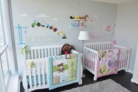 a pastel shared nursery with grey walls, white furniture, colorful images and letters on the wall and pink and blue bedding