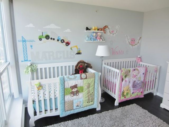 a pastel shared nursery with grey walls, white furniture, colorful images and letters on the wall and pink and blue bedding