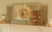a neutral beach mantel with a mirror, a burlap wreath, a box with seashells, starfish and candleholders with starfish