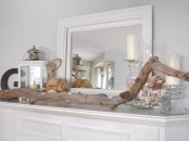 a beach mantel with a driftwood piece, a jar with seashells, candles and candle lanterns