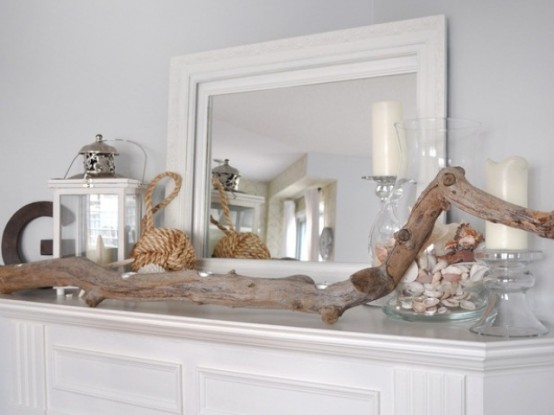 a beach mantel with a driftwood piece, a jar with seashells, candles and candle lanterns