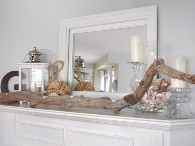 A beach mantel with a driftwood piece, a jar with seashells, candles and candle lanterns