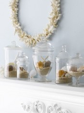 a stylish beach mantel with large clear jars with various seashells and beach sand and a coral wreath over the mantel