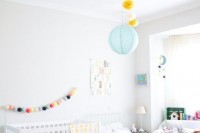 a neutral shared room with colorful lamps, pompom garlands and bright toys and books