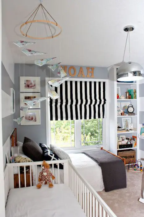 A grey and white nursery, a striped Roman shade, built in shelves, matching beds and a mobile