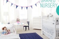 a white shared nursery with touches of navy, a textural rug, a bunting and lots of toys
