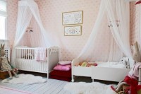 a delightful shared nursery for girls done with pink wallpaper, chic beds, cute toys and fuchsia textiles