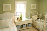 a vintage-inspired green nursery with artworks, elegant beds and a storage unit between them