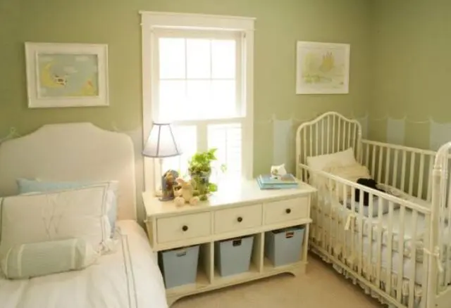 A vintage inspired green nursery with artworks, elegant beds and a storage unit between them