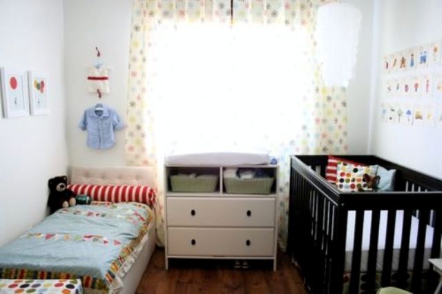 a neutral shared nursery with mismatching beds and colorful and printed bedding