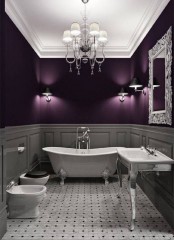 a chic Gothic bathroom with grey paneled and purple walls, vintage appliances and fixtures, a vintage chandelier and a mirror in an ornated frame
