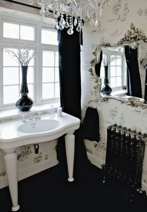 a black and white Gothic bathroom with printed neutral wallpaper, a refined radiator, a sink on legs, a crystal chandelier and a beautiful mirror in an ornated frame