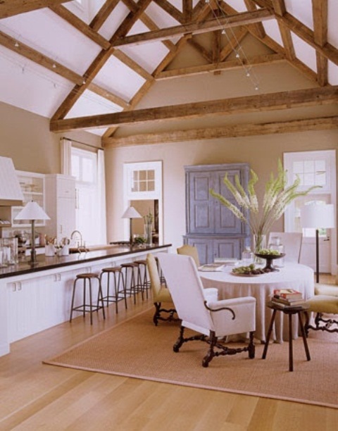 a white and neutral vintage barn kitchen with white cabinets and black countertops, a chalk paint buffet, a round table and mismatching chairs plus wooden beams on the ceiling