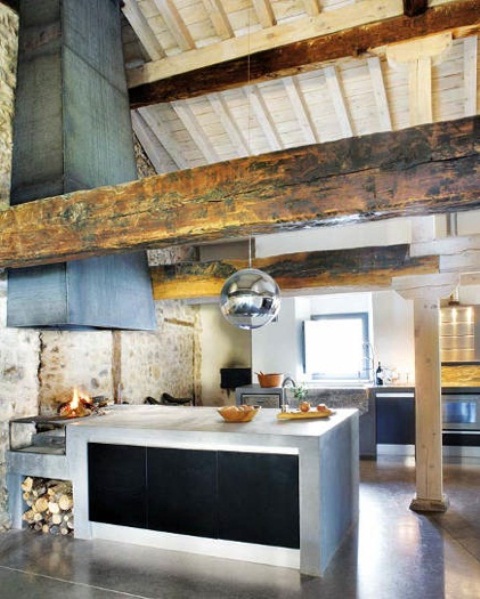 A barn kitchen with a whitewashed ceiling, wooden beams, concrete cabinets, a large hood covered with metal sheets is a cozy wabi sabi space