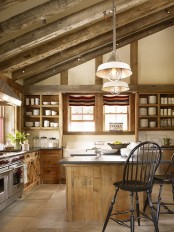 a barn kitchen with reclaimed wooden beams, reclaimed wood cabinets, concrete countertops and vintage black chairs is a cozy space to be