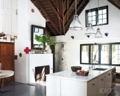 a modern white barn kitchen with a cool kitchen island and glass pendant lamps, a fireplace with a cool screen, a dark wooden ceiling with beams