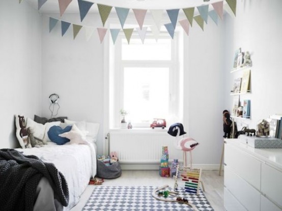 a small Scandi kid's room with sleek white furniture, pastel-colored buntings, ledges with books and artwork, a printed rug and lots of toys