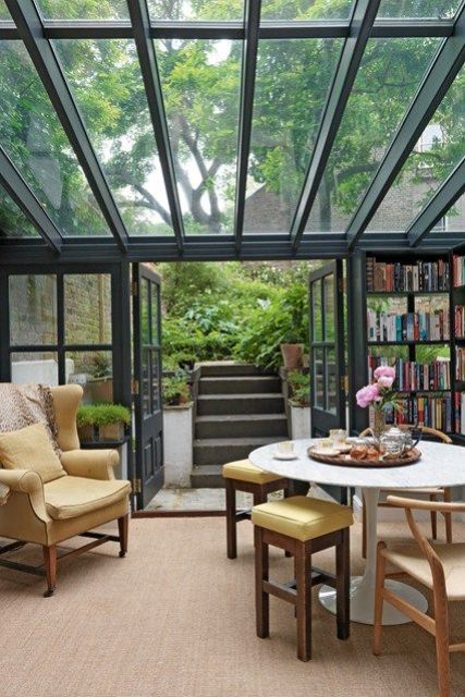 A stylish mid century modern sunroom with simple and elegant furniture, bookshelves and a glazed ceiling and walls