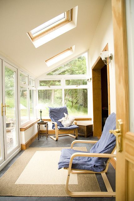 A neutral ultra modern sunroom space with layered rugs, blue chairs and cool skylights to get more natural light