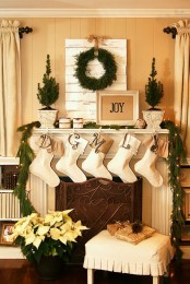 a neutral space with a fir garland, a greenery wreath, stockings, lights and mini potted trees is very chic and cool