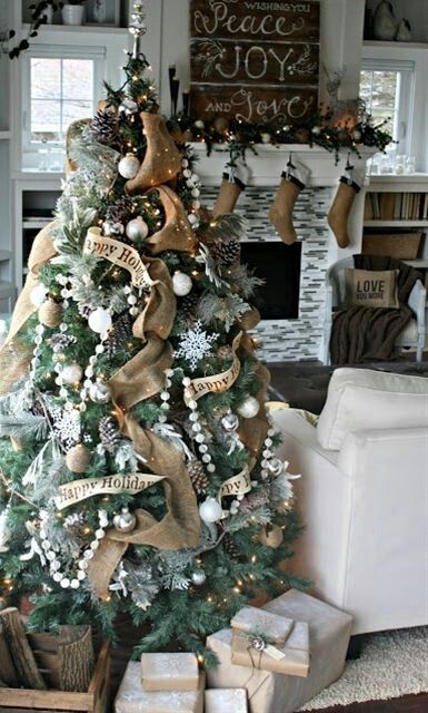burlap stockings, a fir garland with silver ornaments, a Christmas tree with burlap ribbons, pompoms, silver and white ornaments for a rustic holiday feel in the room