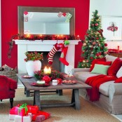 a bright red and neutral Christmas living room with a greenery and berry garland on the mantel, funny red stockings, a Christmas tree with lights and red ornaments, red pillows and blankets plus red teaware on the table