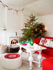 a red and white Scandinavian Christmas living room with matching holiday decor – a Christmas tree with red and white ornaments, a red and white fabric banner over the space