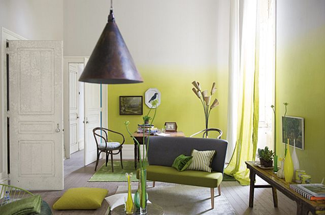 An eye catchy living room with ombre neon yellow walls, a small dining zone with vintage furniture, a grey loveseat and neon green and yellow pillows and curtains